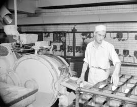 [Man removing shaped bread dough from a machine and placing it in loaf plans]