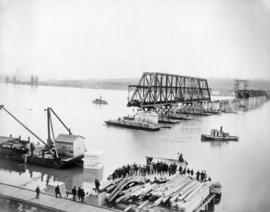 [A crowd gathers to watch a span of the bridge being floated into place]