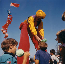 Performer on stilts with children on P.N.E. grounds