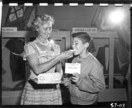 Woman feeds boy award-winning baking entry in 1957 P.N.E. Home Arts competition