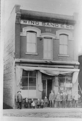 Yip Sang with children and unidentified men in front of Wing Sang Company building at 51 East Pen...
