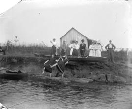 [Men and women assembled near shore at Linn's cottage]