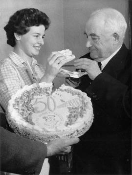 [Woman feeding] Major J.S. Matthews Golden Jubilee bank account cake 1909-1959