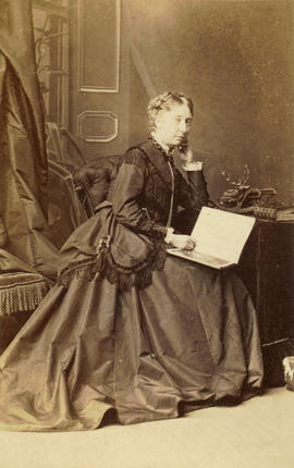[Studio portrait of woman seated at a table with a large book in her lap]