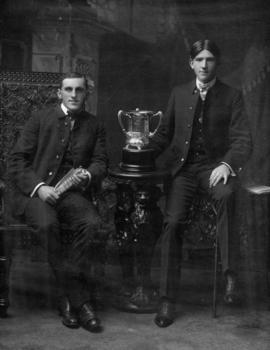 Portrait of two young Vancouver firemen seated beside silver trophy