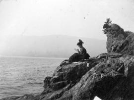 [Woman sitting on rock formation known as Siwash Rock's wife, sketching]