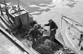 [Two men repairing nets on a boat]