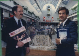 Mike Harcourt and unidentified man hold up books in front of display case