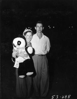 Man and woman holding prize stuffed bear won at Jack's stand in P.N.E. Gayway