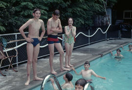 [Children in and on the deck of an outdoor pool]