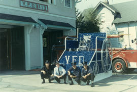 [Four firefighters in front of wheelchair float built for parade]