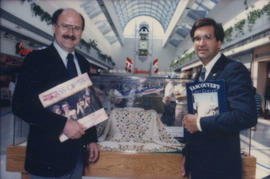 Mike Harcourt and unidentified man hold up books in front of display case