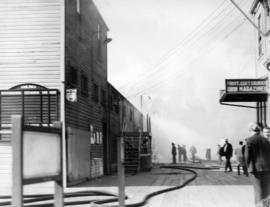 [View of smoke and buildings and fighters with hose during Union Steamship dock fire]