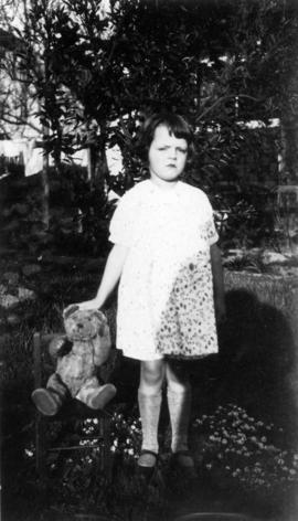 [Mary Louise Taylor standing in yard with teddy bear]