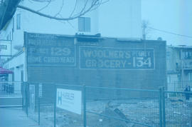 [Signs for C.H. Moodie Fresh Meats and Fish and Woolner's Grocery uncovered on the east side of t...
