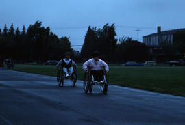 [Two people in wheelchairs on running track]