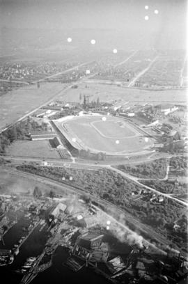 Aerial view of Hastings Park, looking east, with log booms on south shore of Burrard Inlet in for...