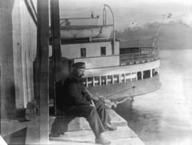 [An unidentified man sitting on a dock near a ferry]