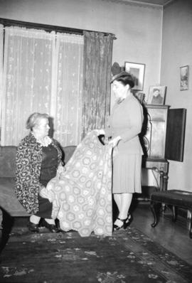 [Miss Richardson in a house showing a blanket to a woman, taken for Nelson's laundry]