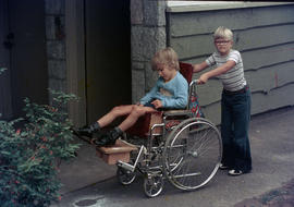 [Boy pushing boy in wheelchair]