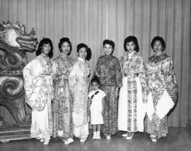 Six women and a young girl wearing traditional-style Chinese clothing and posing with a dragon st...