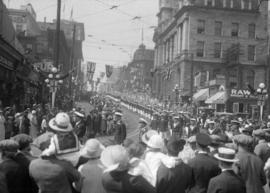 Military parade turning onto Cordova St. with a crowd watching