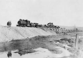 Locomotive with railway cars dumping gravel over timber trestle with house in background : March ...