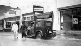 Two men in flooded street in front of Penticton furniture store and Hanlon's china shop