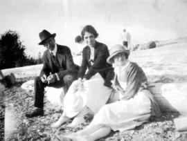 [L.D. Taylor sitting on beach at Summit Lake with two unidentified women]