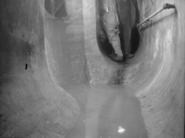 Men standing in opening of concrete sewer tunnel