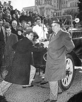 [Mayor Fred Hume and James Melton (pushing vintage car) with crowd looking on outside City Hall]