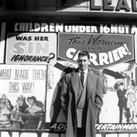 [Joseph Selsey standing in front of adult entertainment poster]