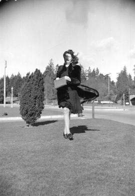 [Miss Isle Sternberg walking along road at entrance to Stanley Park on a breezy day]