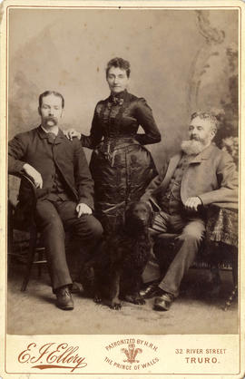 Portrait of a woman standing between two seated men with dog