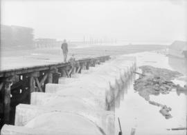 Two men standing on a pier beside a sewer pipe