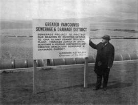 Alderman Halford Wilson standing by signage at English Bay for Fiberglass pipe for sewerage project