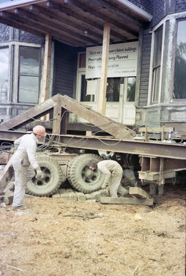 [Detail view of moving crew and Hodson House raised on wheels during house relocation]