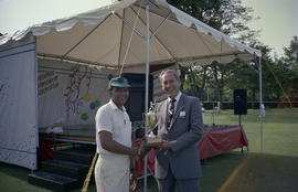 Two unidentified men with trophy in front of Centennial event tent