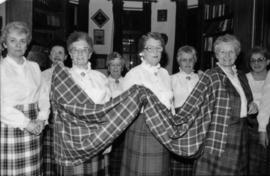 Group of women wearing tartan skirts holding a piece of the Centennial tartan fabric