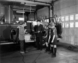 [Vancouver Fire Department staff member explaining tools to interviewer and boy scouts]