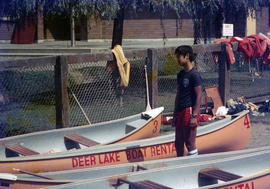 [Boy standing by canoes at Deer Lake]