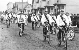 [Japanese men in mourning sashes ride bicycles to the memorial service for King Edward VII]