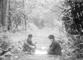 [Two men playing cards in the middle of a logging road in Stanley Park]