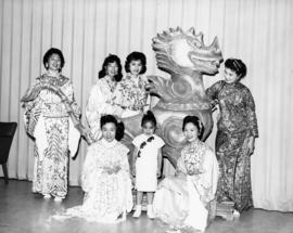 Six women and a young girl wearing traditional-style Chinese clothing and posing with a dragon st...