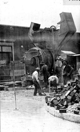[Men with large cement machine] laying concrete base [for road work along Main St.]