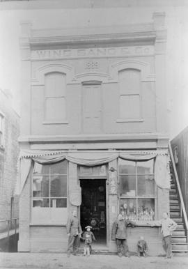 Yip Sang with children and unidentified men in front of Wing Sang Company building at 51 East Pen...