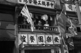 [Men watching VJ celebrations from balcony in Chinatown]