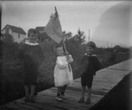 Three children standing on a boardwalk holding a dominion flag