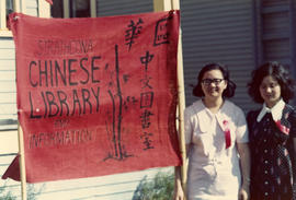 Two young women standing with sign for the Strathcona Chinese Library and Information