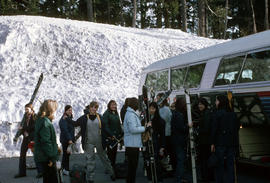 [Female skiers beside snowbank and bus]